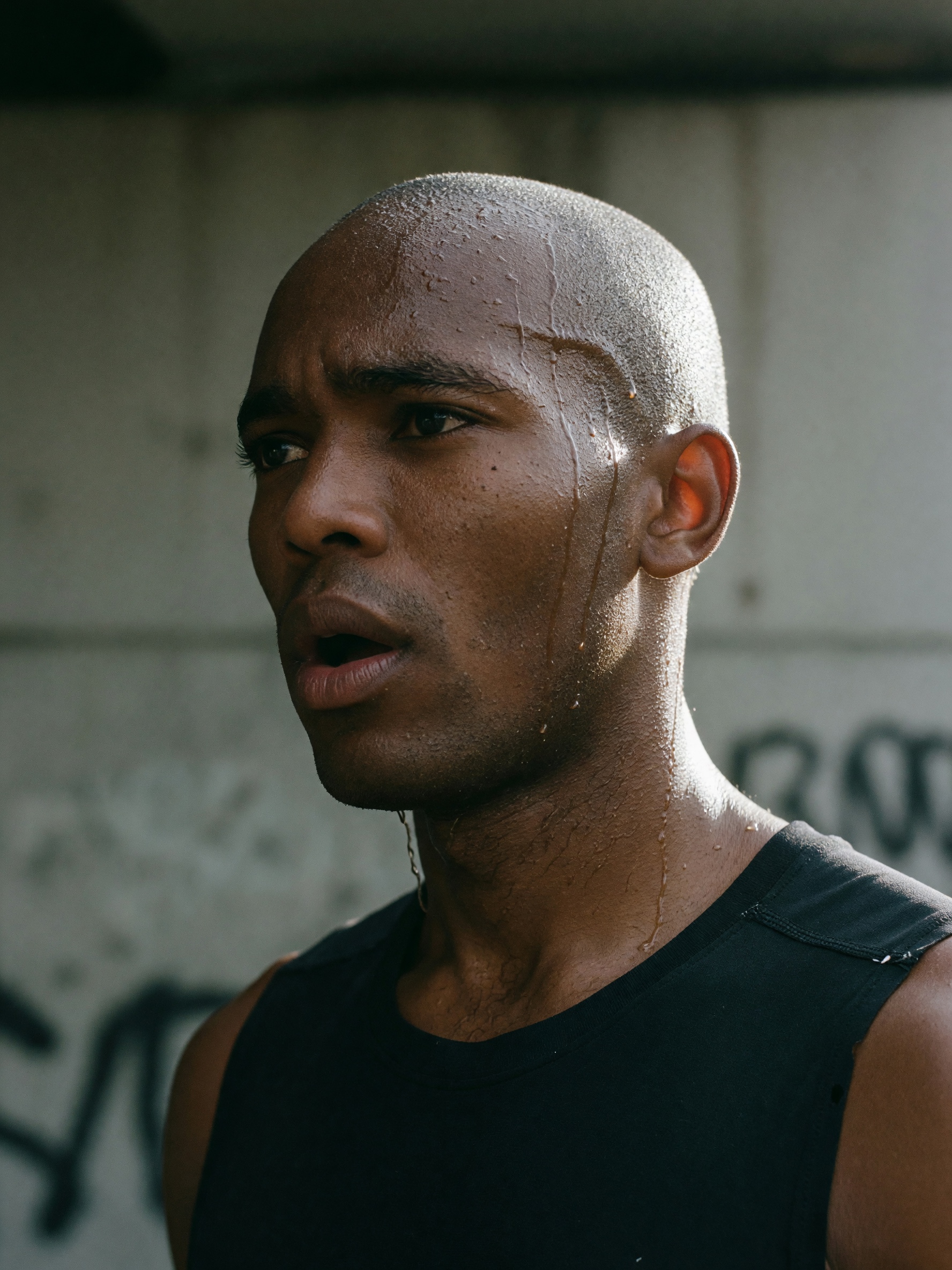 Close portrait of a bald man in a black tank top in front of a graffiti wall