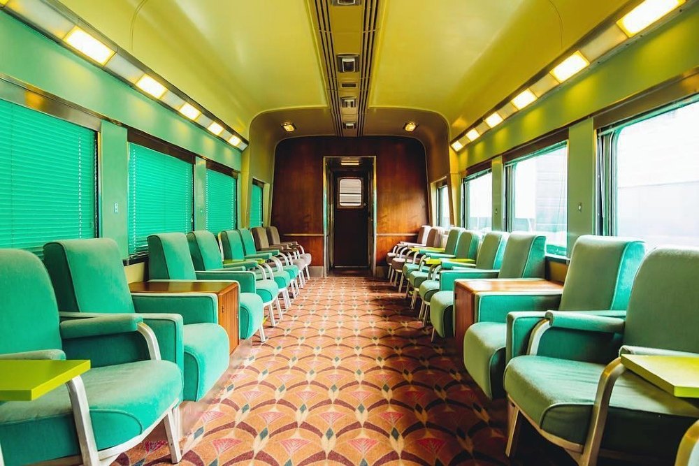 The interior of a 1970s train carriage with green seats and a patterned floor