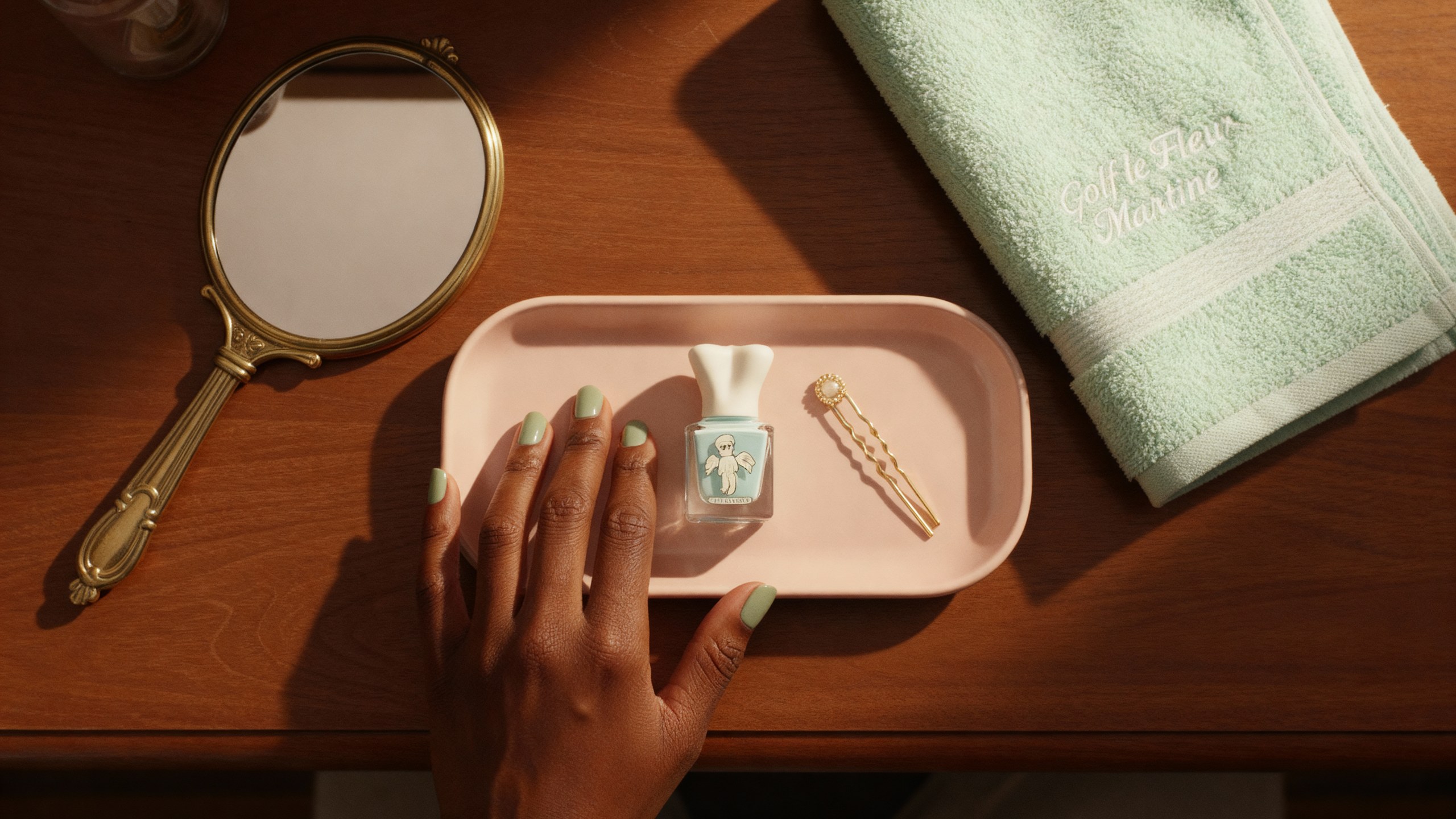 A hand with pale blue nails resting on a blush lacquer tray, the polish bottle beside a hand mirror and a mint towel