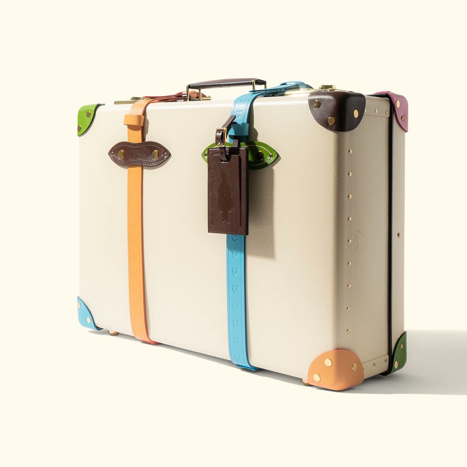 The cream Golf le Fleur suitcase with pastel leather straps, photographed on white
