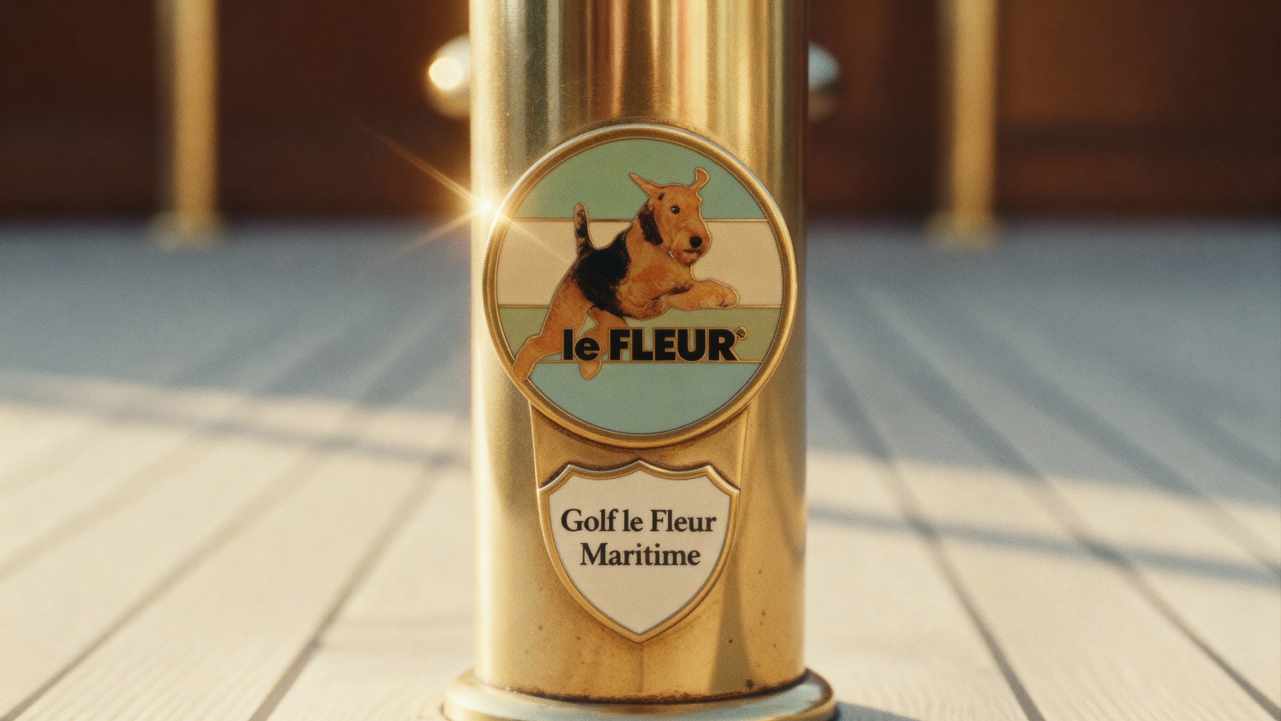 A polished brass bollard on a sunlit deck carrying an enamel le Fleur badge reading Golf le Fleur Maritime