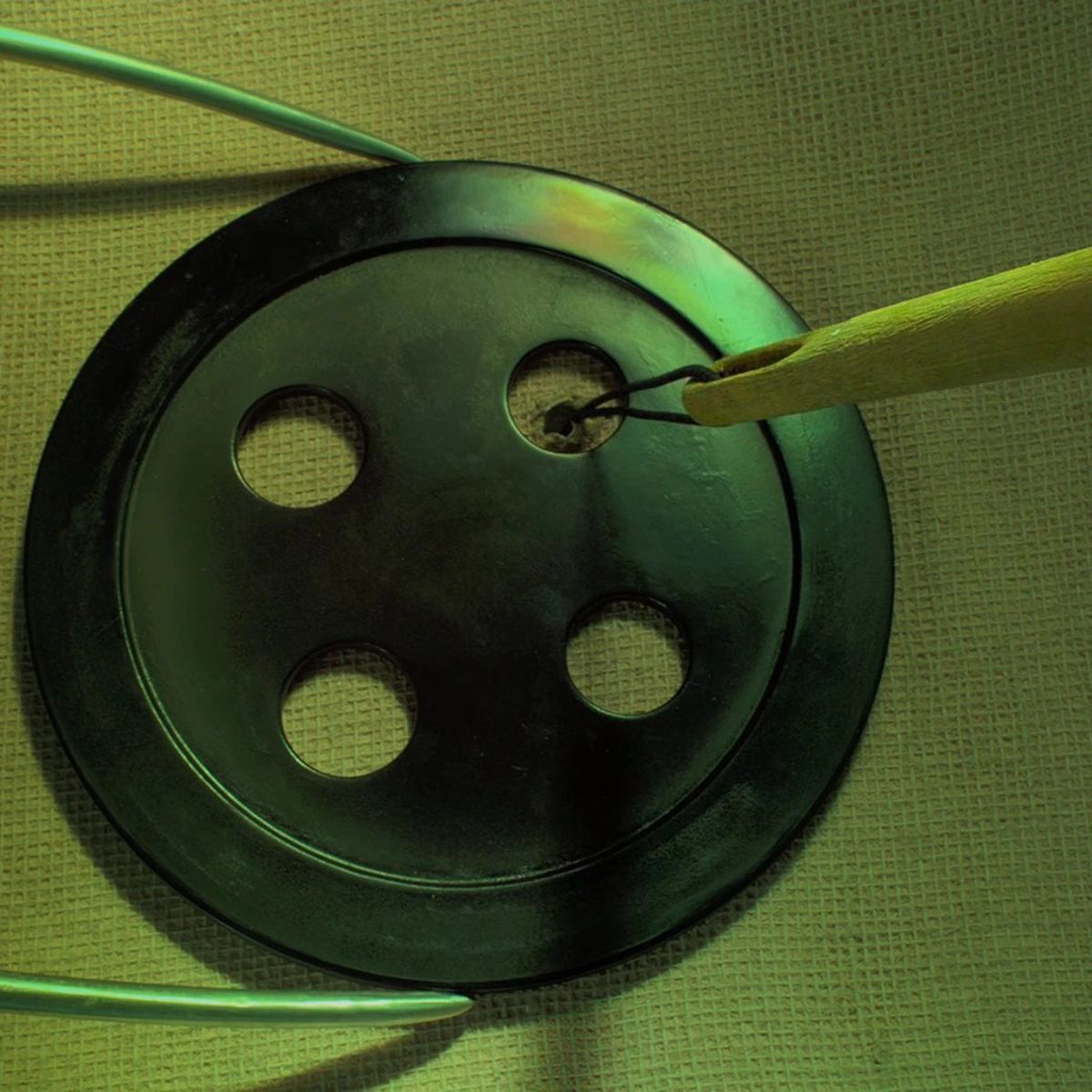 Coraline: a button being sewn on in close-up, the weave of the fabric visible