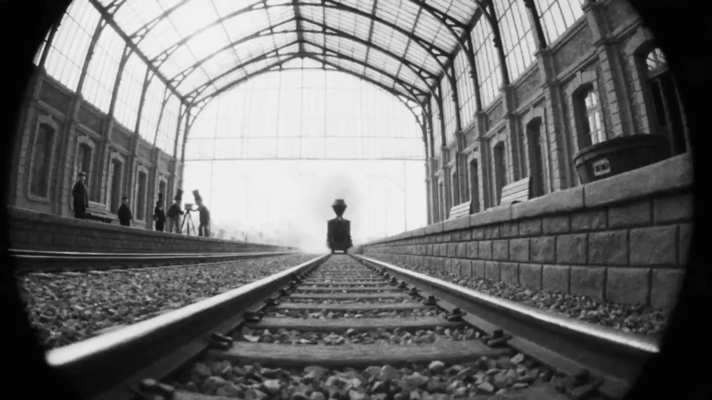 A steam train arrives head on down the platform, in black and white